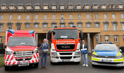 Michael May, Geschäftsführer des GUV OL, und Henning Wolff, stv. Geschäftsführer, stellen die Karte für Ersthelfende vor dem Alten Oldenburgischen Landtag vor, flankiert von Fahrzeugen des Rettungsdienstes, der Polizei und der Feuerwehr Oldenburg