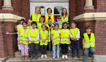 Theresa Wieting übergibt die Sicherheitswesten an Melanie Fuchs, Lehrkraft, und Erstklässlerinnen und Erstklässler der Grundschule Röwekamp